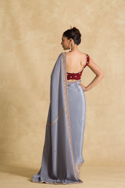 Woman in a grey embroidered saree and maroon blouse with back open design, studio background