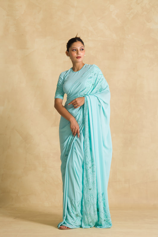 Woman in light blue embroidered saree posing against beige background