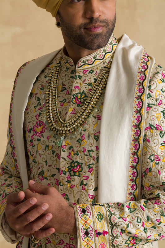 Man in floral embroidered sherwani with layered pearl necklace and cream dupatta
