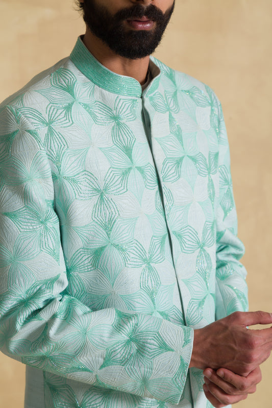 Man in mint green floral jacquard sherwani with mandarin collar, beige background