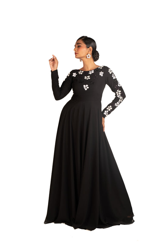 Woman in long black gown with white floral embroidery and statement earrings on white background